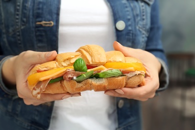 Photo of Woman holding tasty croissant sandwich, closeup