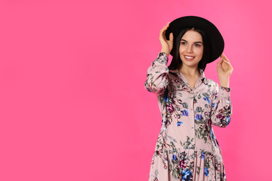 Young woman wearing floral print dress and stylish hat on pink background. Space for text