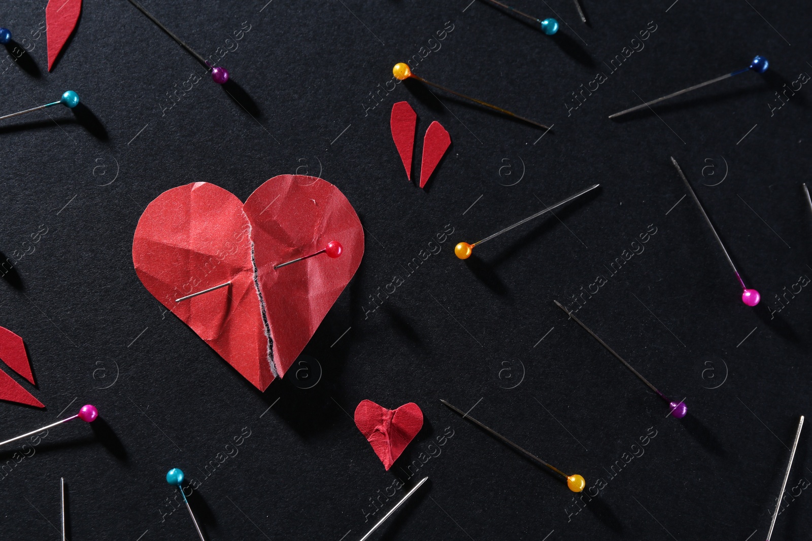 Photo of Halves of torn paper heart connected by sewing pin among other ones on black background, flat lay. Relationship problem concept