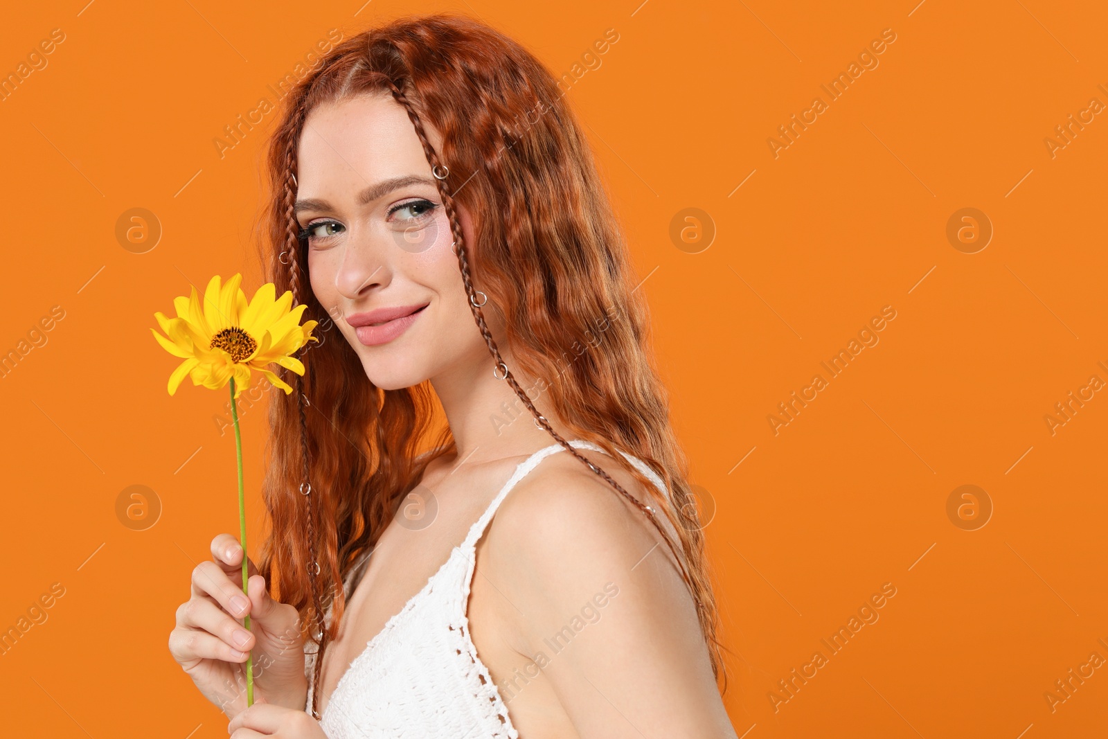 Photo of Beautiful young hippie woman with sunflower on orange background, space for text