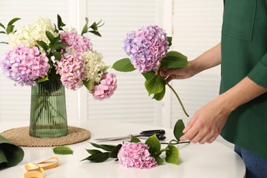 Photo of Woman making bouquet with beautiful hydrangea flowers at table indoors, closeup. Interior design element