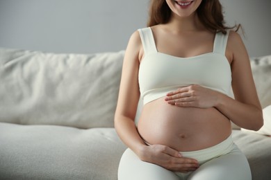 Pregnant woman touching her belly indoors, closeup