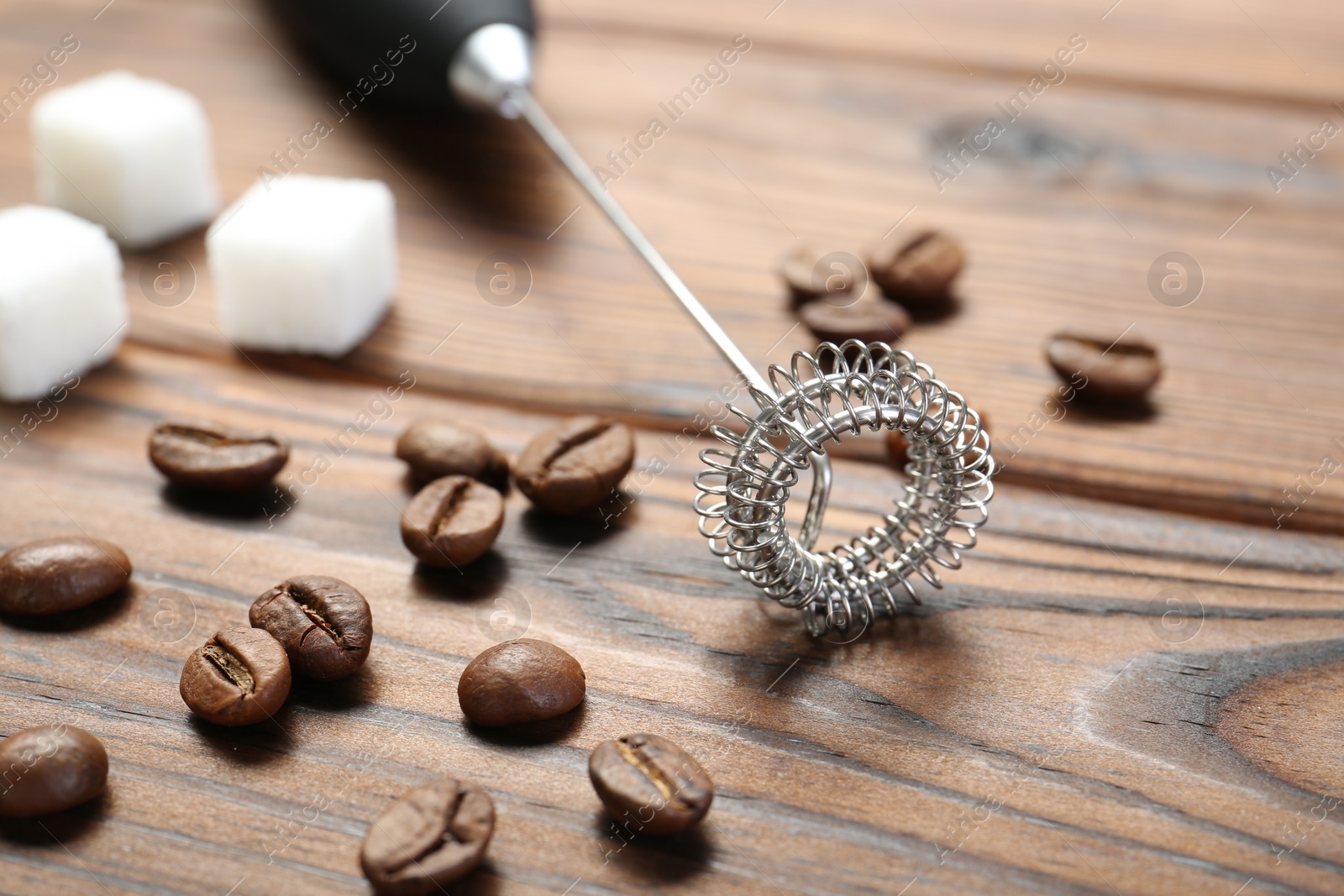 Photo of Black milk frother wand, sugar cubes and coffee beans on wooden table, closeup