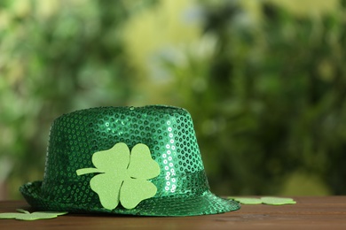 Photo of Green sequin hat with clover leaf on wooden table against blurred background, space for text. St Patrick's Day celebration