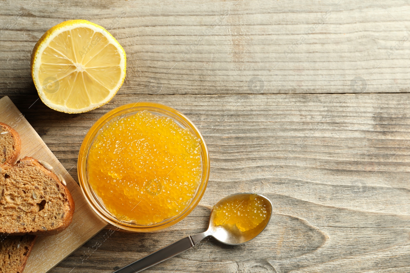 Photo of Fresh pike caviar in bowl, lemon and bread on wooden table, flat lay. Space for text