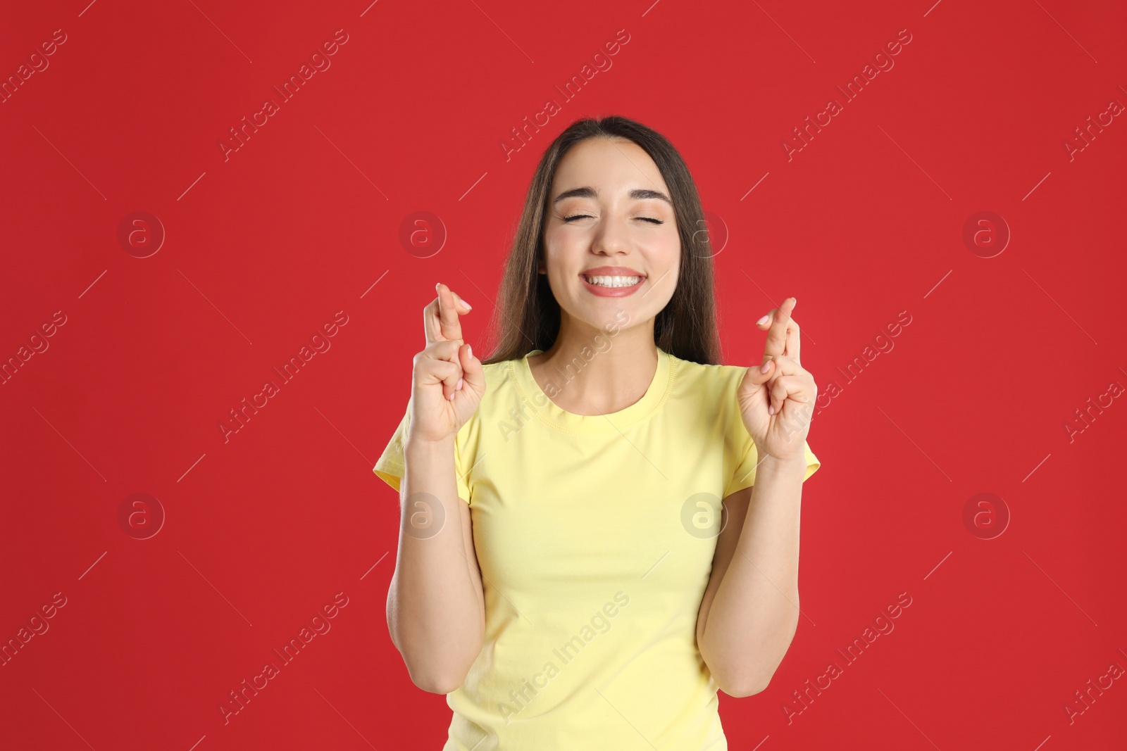Photo of Excited young woman holding fingers crossed on red background. Superstition for good luck