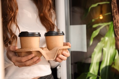Photo of Woman holding paper coffee cups indoors, closeup. Space for text