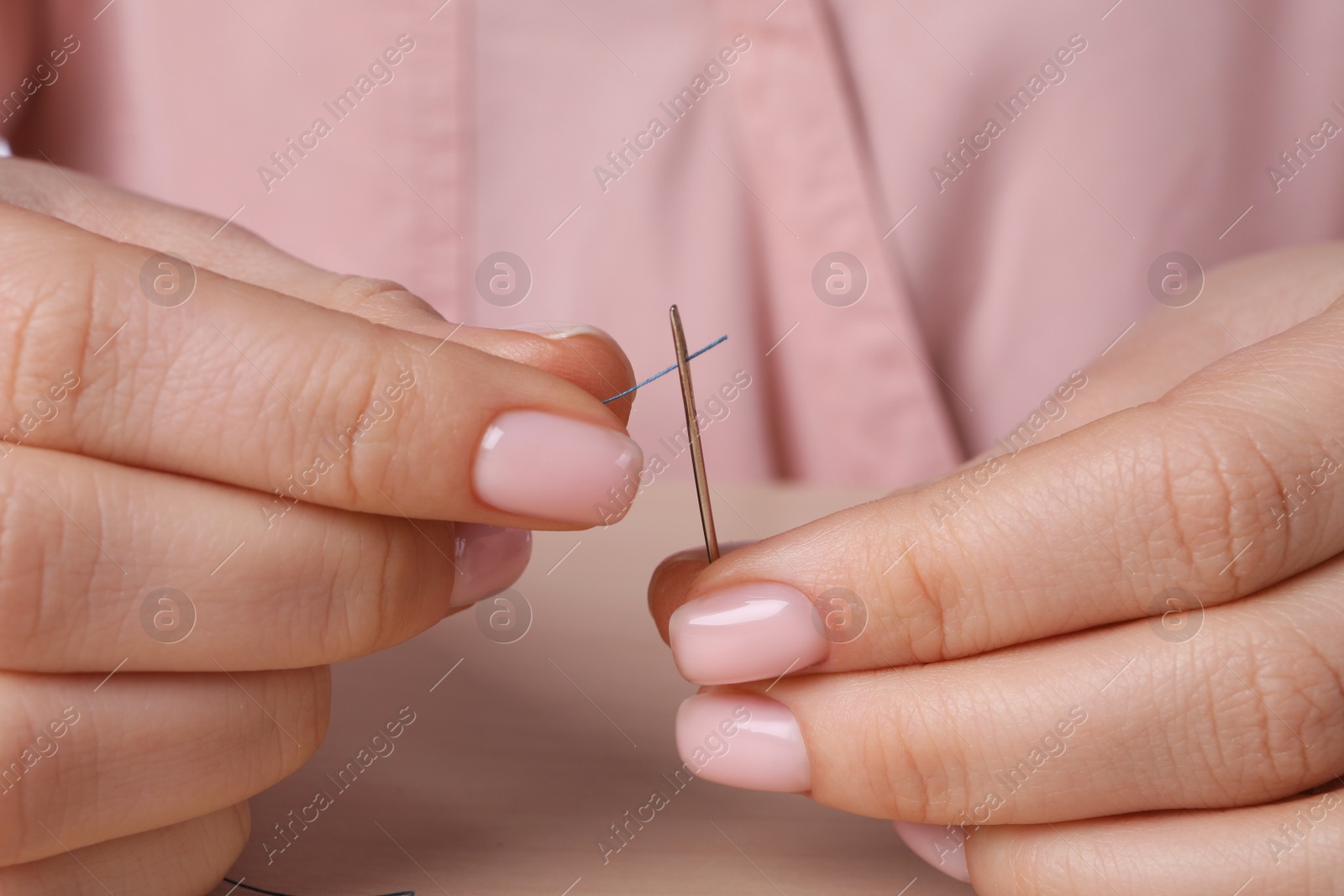 Photo of Woman threading sewing needle at table, closeup