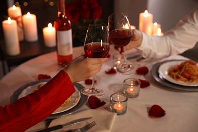 Photo of Couple clinking glasses of wine indoors, closeup. Romantic dinner