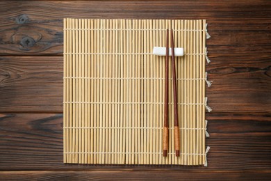 Photo of Bamboo mat with pair of chopsticks and rest on wooden table, top view