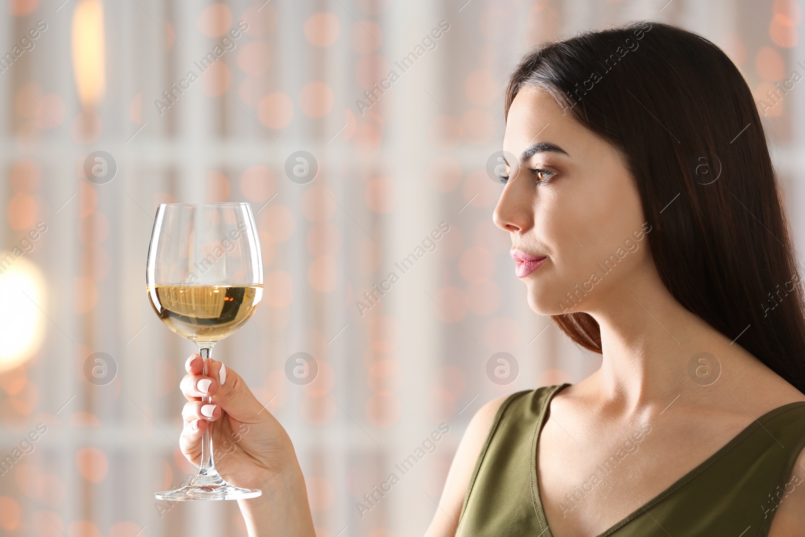 Photo of Beautiful young woman with glass of luxury white wine indoors. Space for text