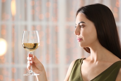 Photo of Beautiful young woman with glass of luxury white wine indoors. Space for text