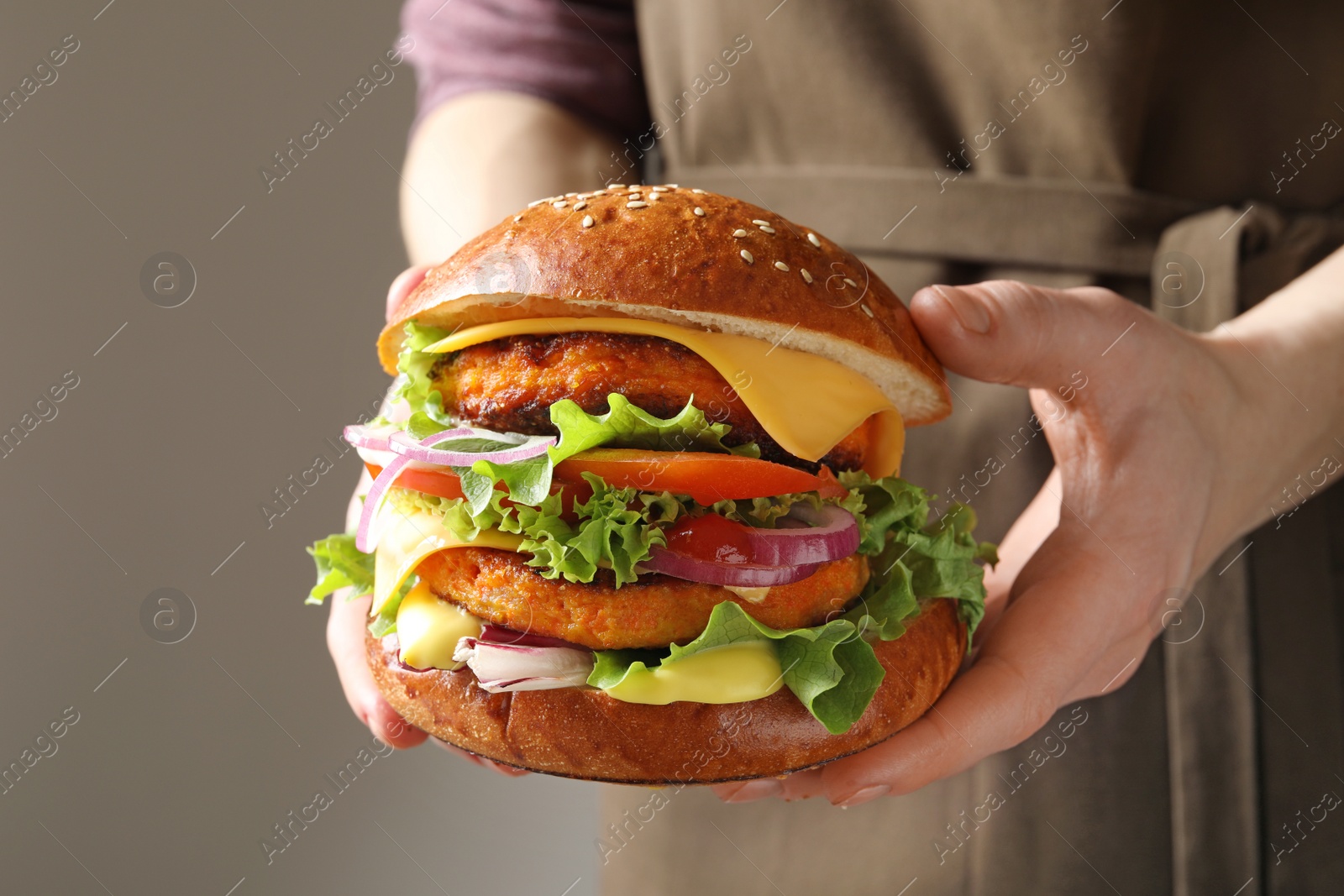 Photo of Woman holding tasty vegetarian burger on grey background, closeup