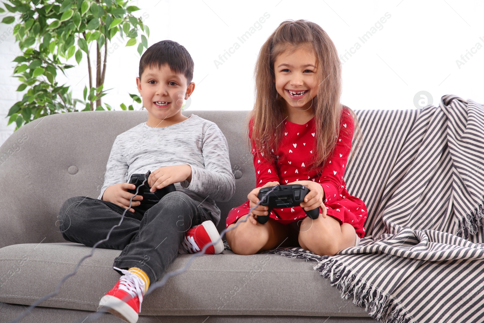 Photo of Cute children playing video game on sofa in living room