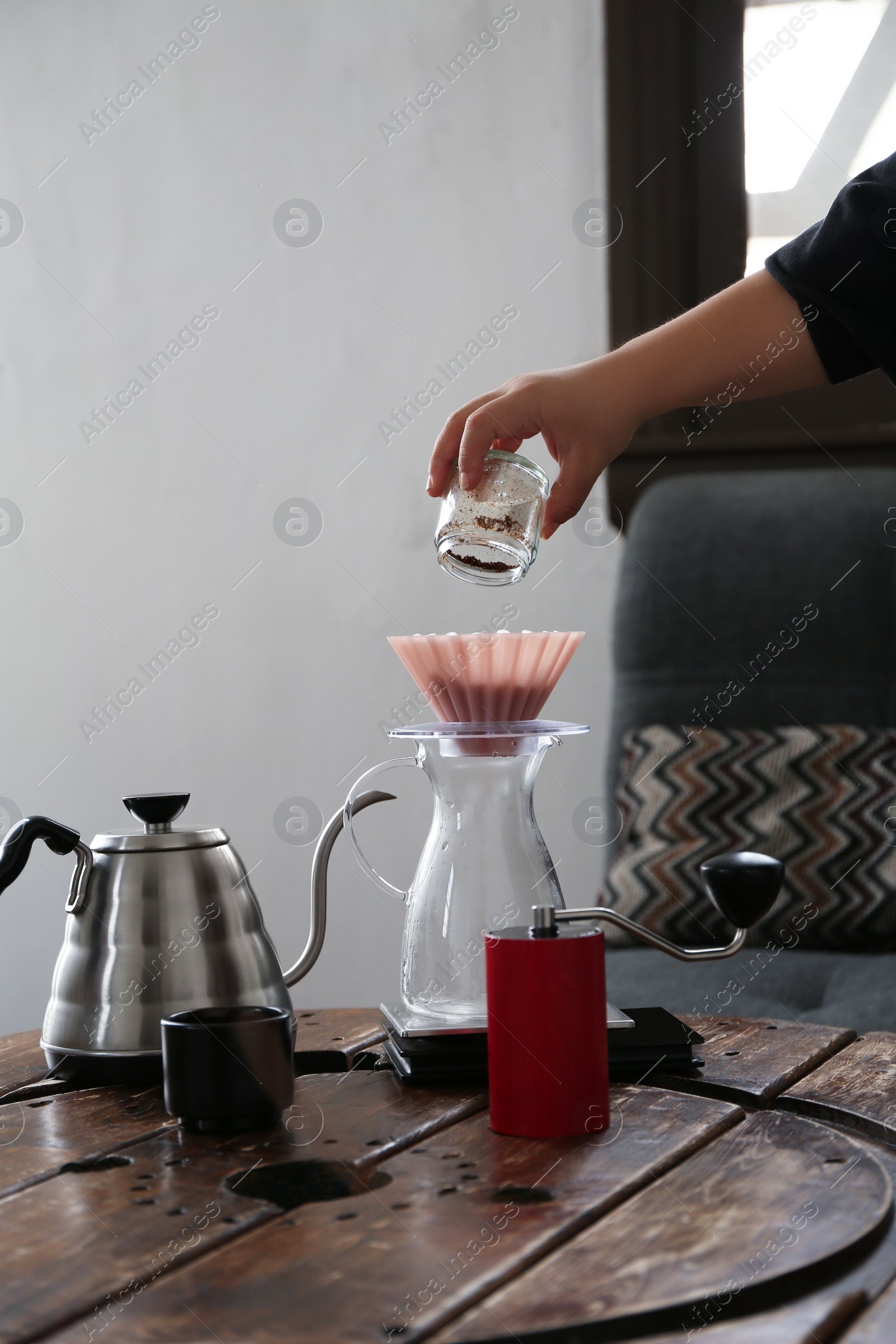 Photo of Barista putting coffee into jug with wave dripper at wooden table in cafe, closeup