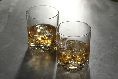 Photo of Whiskey with ice cubes in glasses on grey marble table