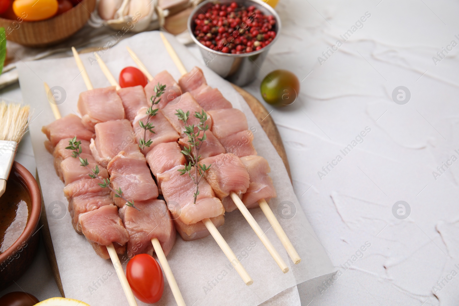 Photo of Skewers with cut raw meat, thyme and tomatoes on light textured table, closeup. Space for text