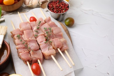 Photo of Skewers with cut raw meat, thyme and tomatoes on light textured table, closeup. Space for text