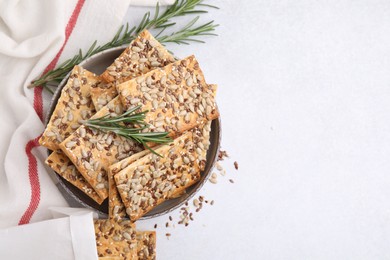 Photo of Cereal crackers with flax, sunflower, sesame seeds and rosemary in bowl on white table, top view. Space for text