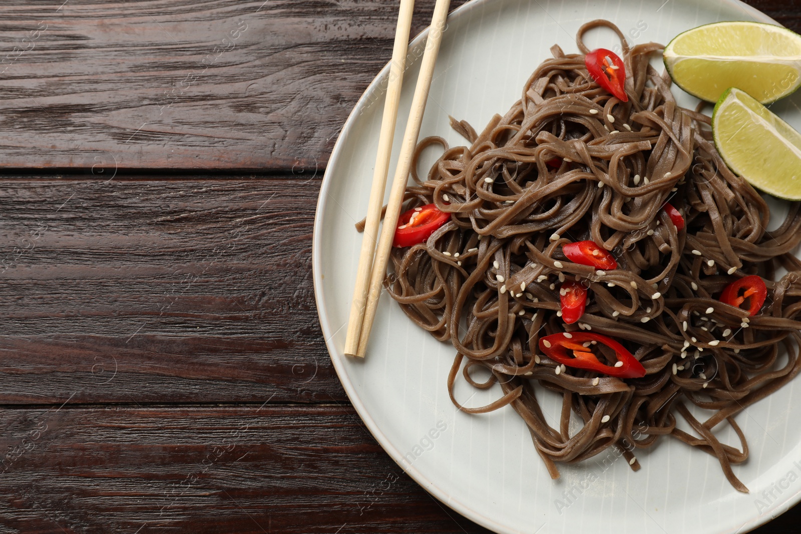 Photo of Tasty buckwheat noodles (soba) with chili pepper, lime and chopsticks on wooden table, top view. Space for text