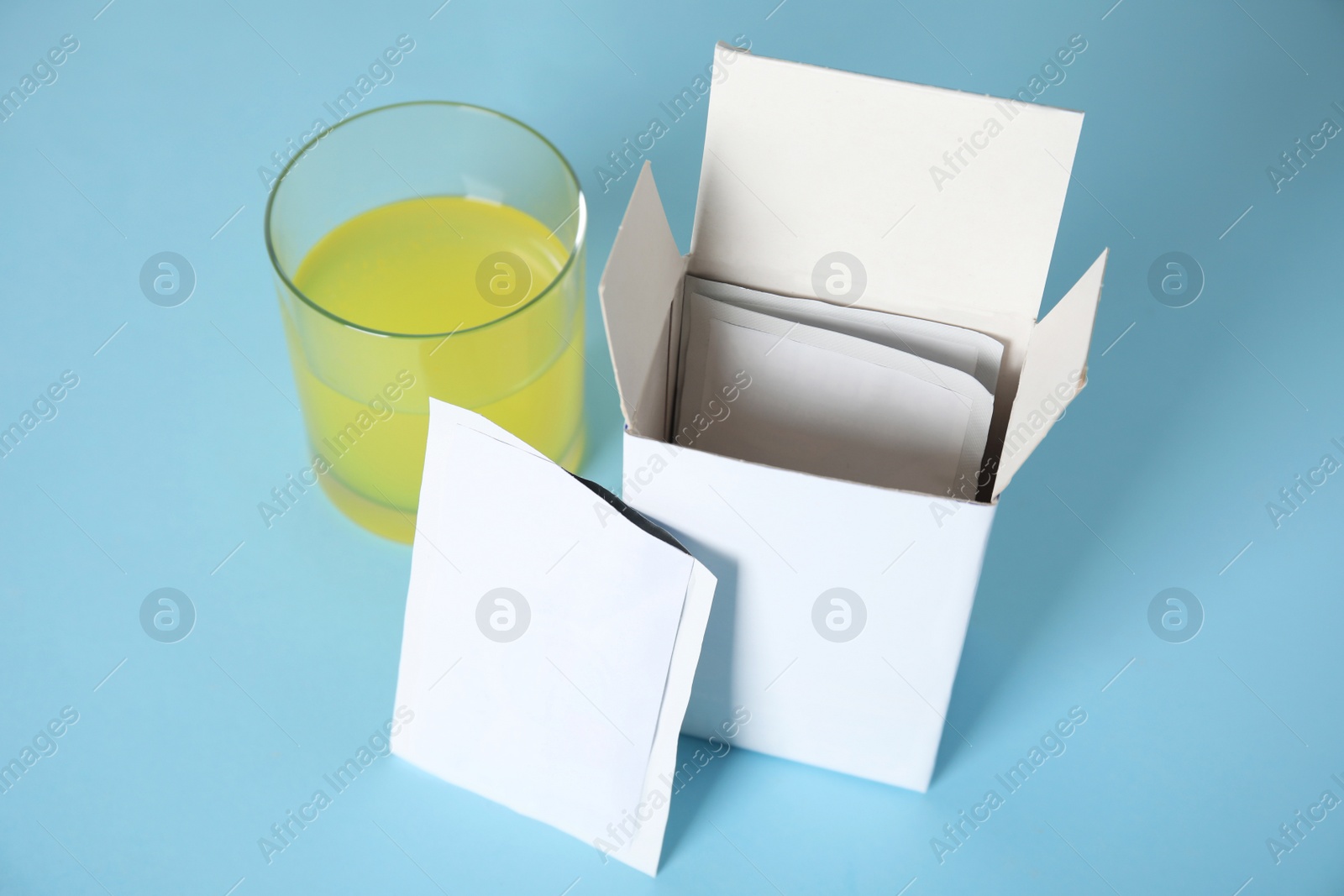 Photo of Box with sachets and glass of dissolved medicine on turquoise background