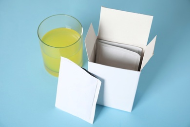 Photo of Box with sachets and glass of dissolved medicine on turquoise background