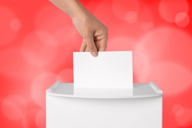 Man putting his vote into ballot box on red background, closeup