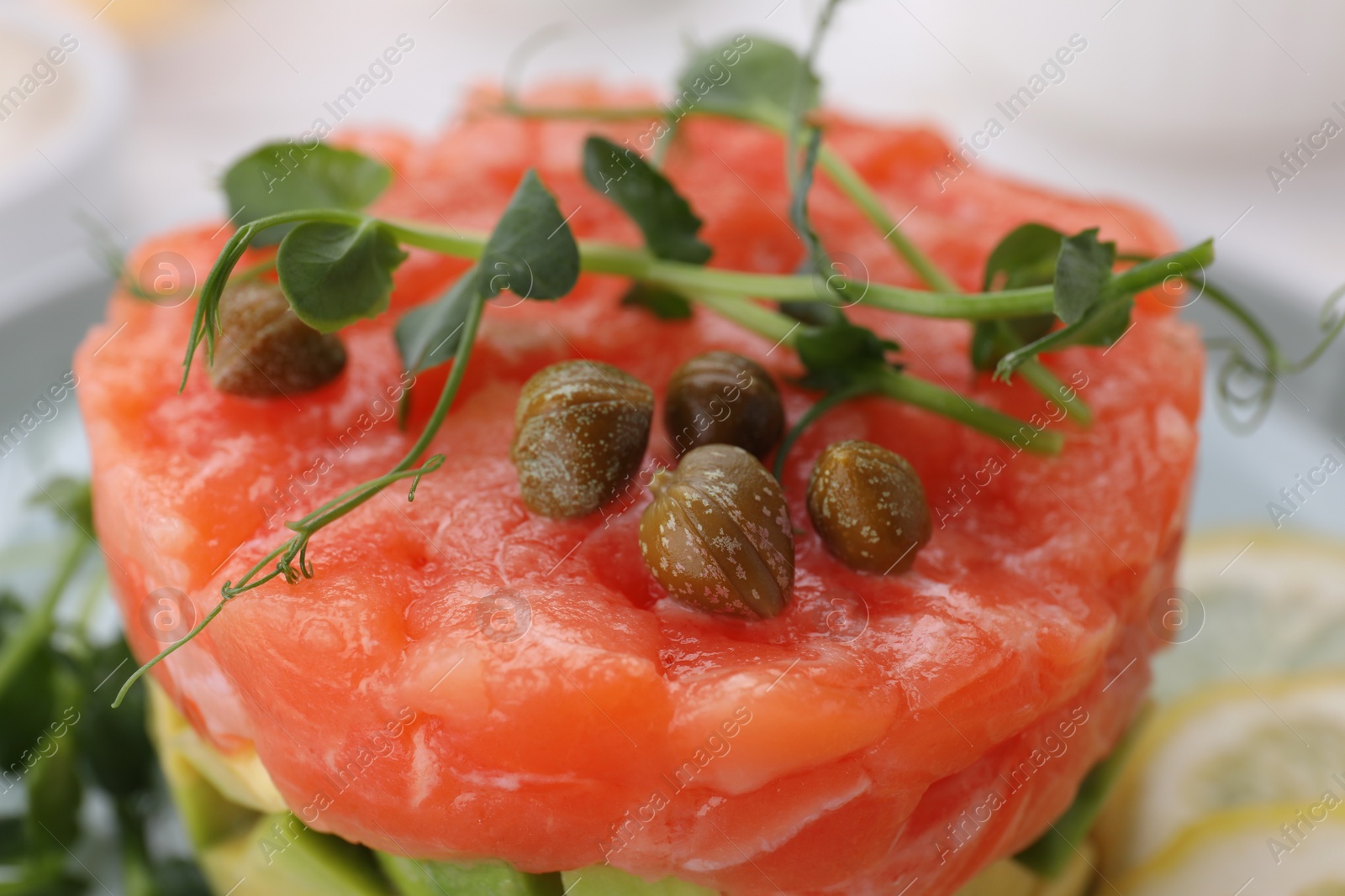 Photo of Tasty salmon tartare with capers and microgreens on plate, closeup