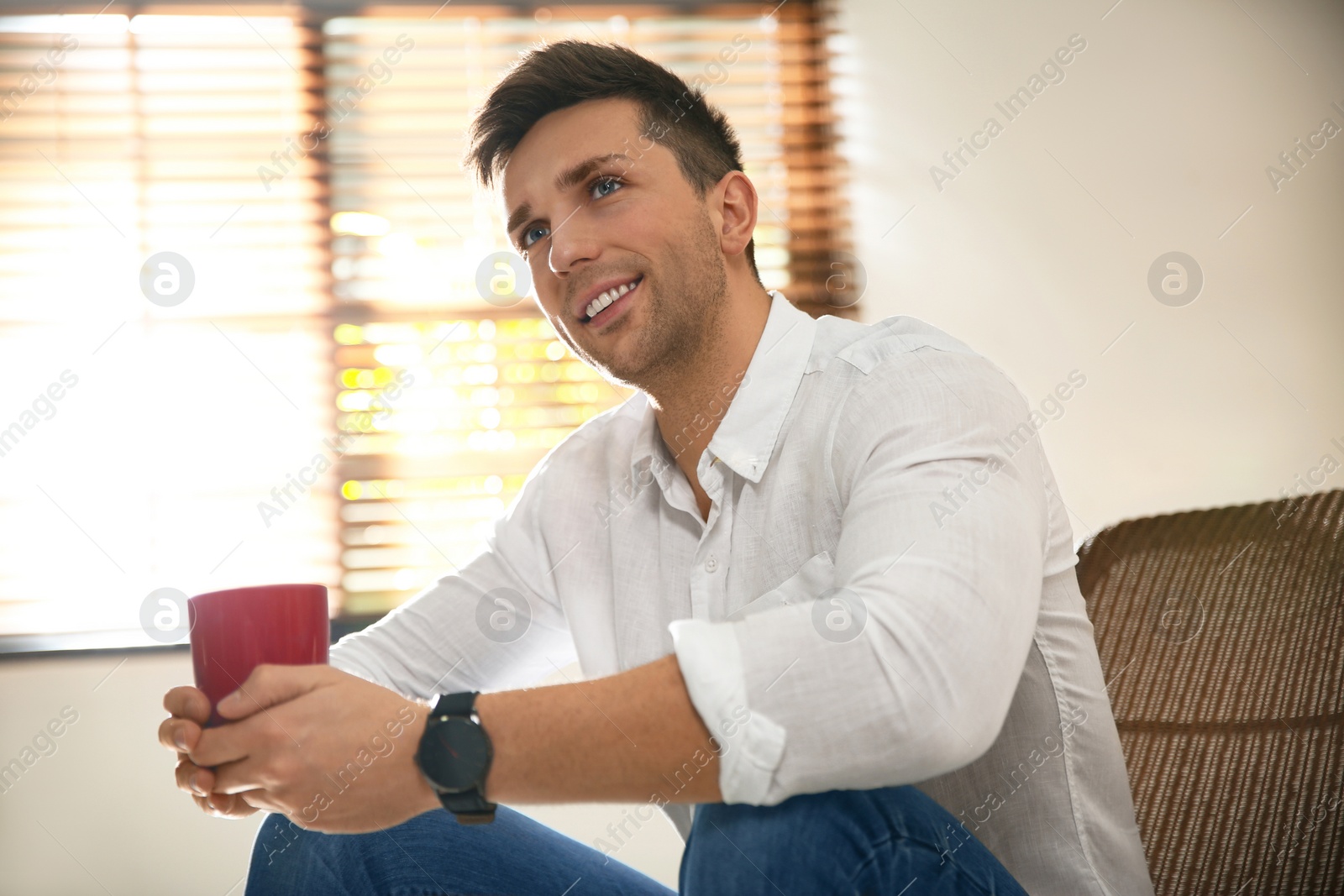 Photo of Young man with cup of drink relaxing near window at home