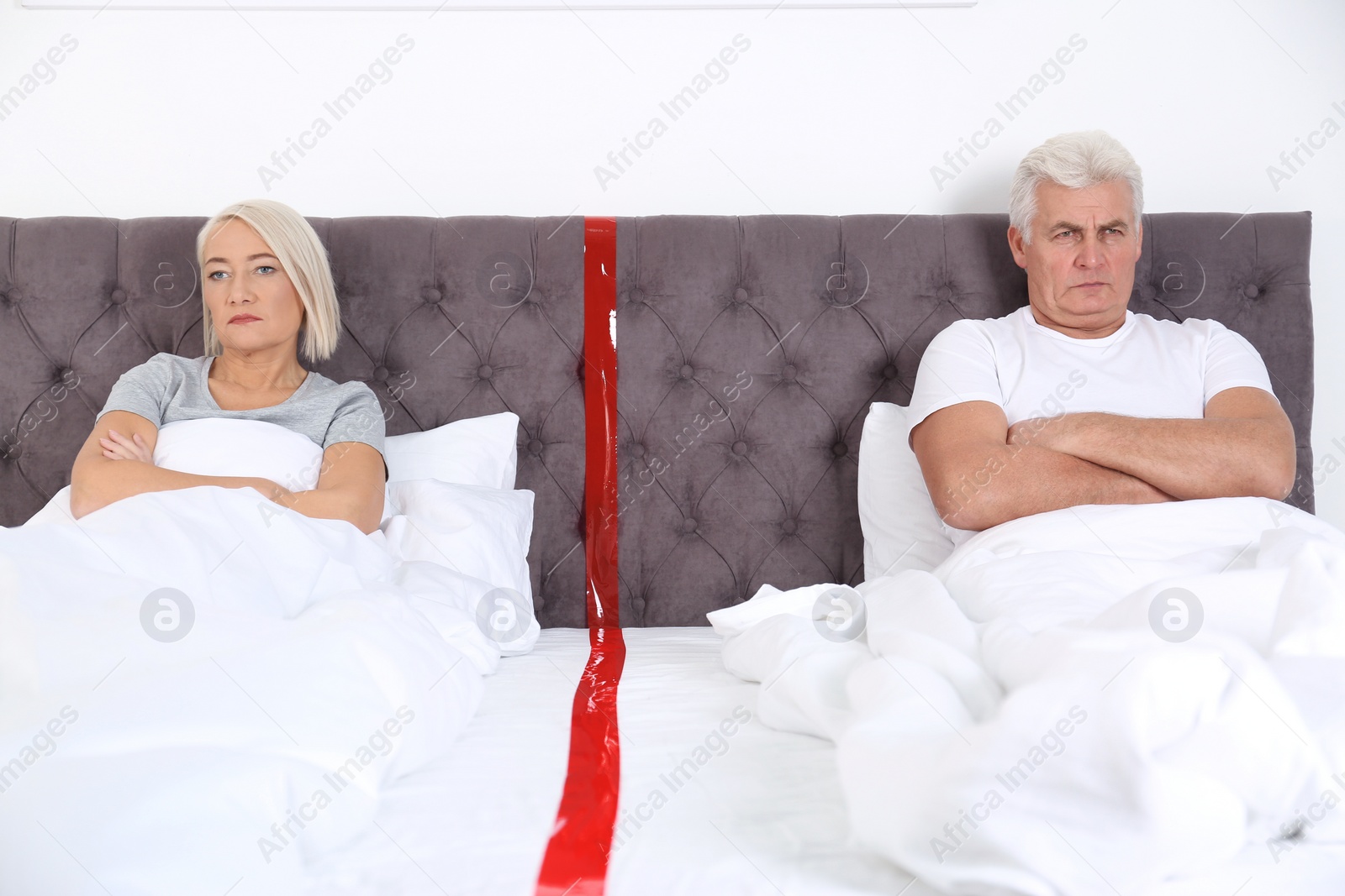 Photo of Upset mature couple with relationship problems lying separately in bed at home