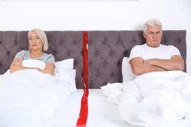 Upset mature couple with relationship problems lying separately in bed at home
