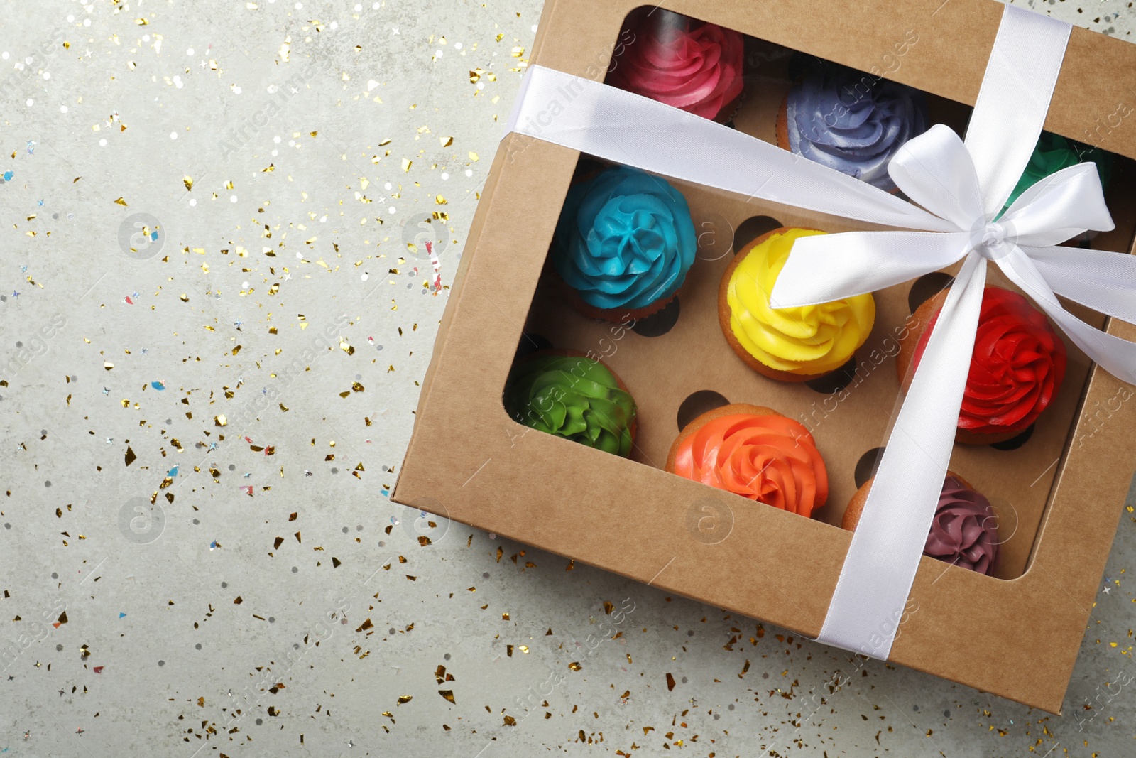 Photo of Box with delicious colorful cupcakes and confetti on light grey table, flat lay. Space for text