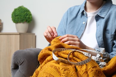 Photo of Woman sewing sweater with needle at home, closeup
