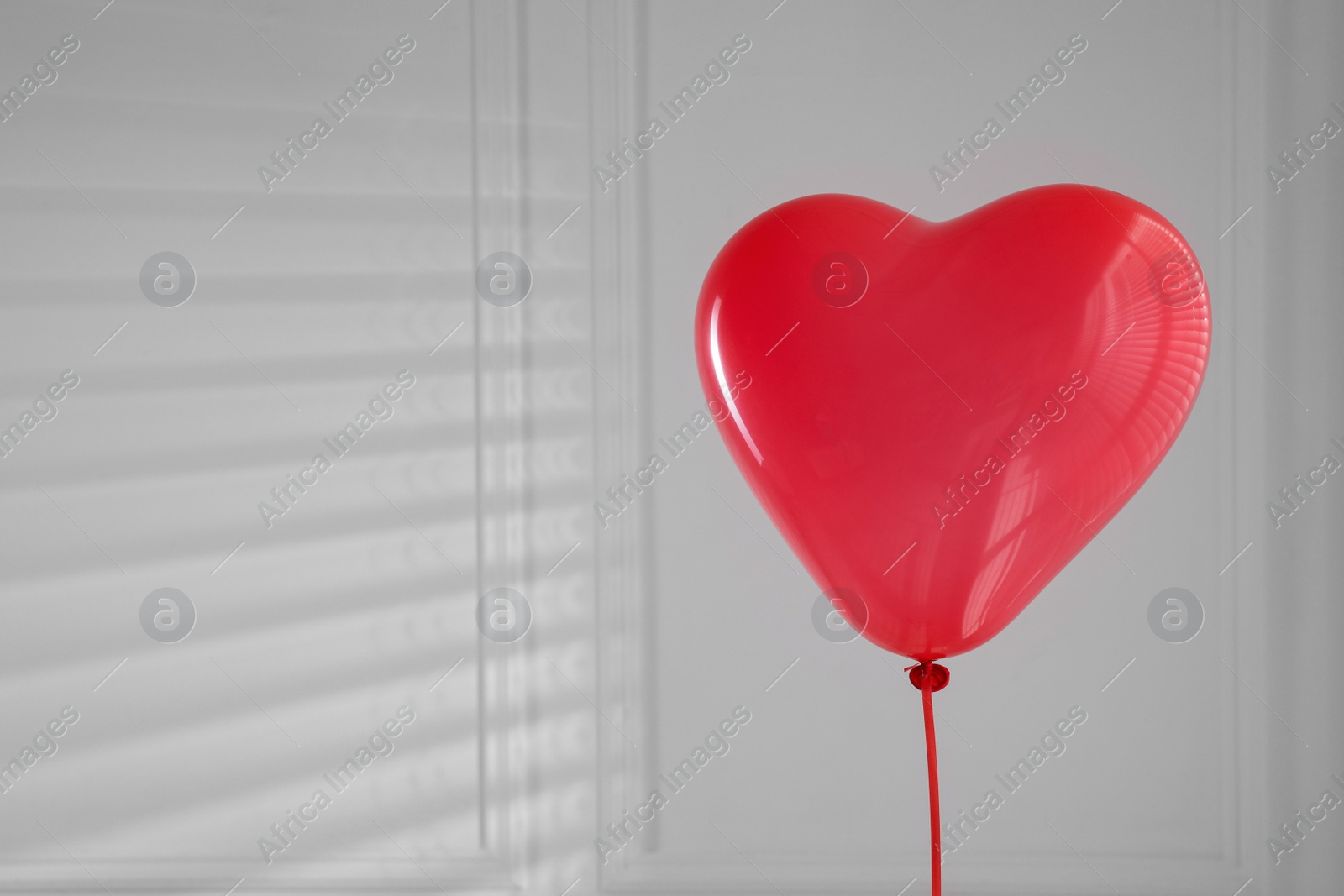 Photo of Festive heart shaped balloon in light room. Space for text