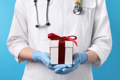 Photo of Doctor holding gift box on light blue background, closeup. Medical present