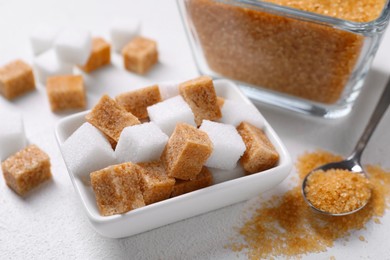 Photo of Bowls and spoon with different types of sugar on white table, closeup