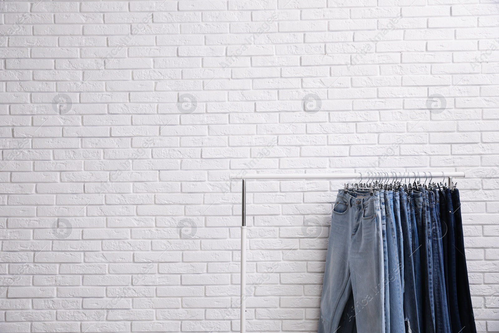 Photo of Rack with stylish jeans near brick wall. Space for text