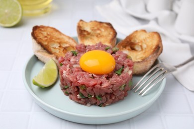 Photo of Tasty beef steak tartare served with yolk, toasted bread and lime on white tiled table