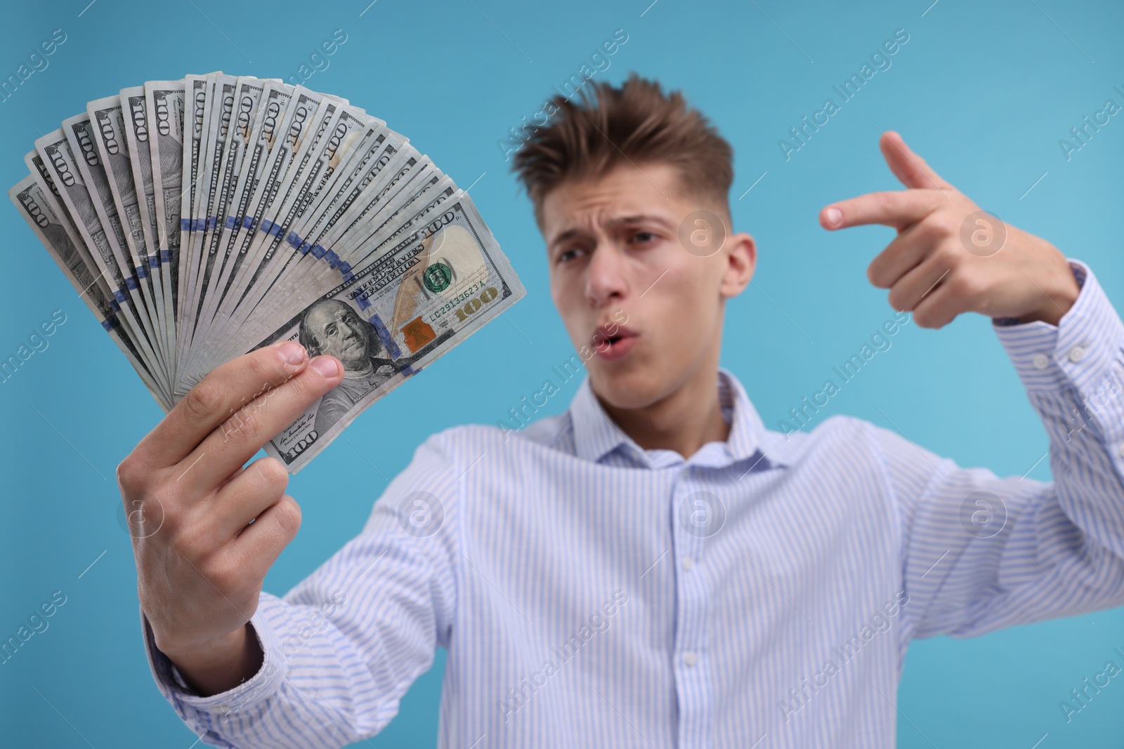 Photo of Handsome man pointing at dollar banknotes on light blue background, selective focus