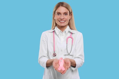 Photo of Doctor with stethoscope holding pink ribbon on light blue background. Breast cancer awareness