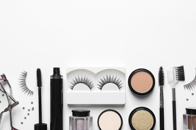 Composition with false eyelashes and other makeup products on white background, top view