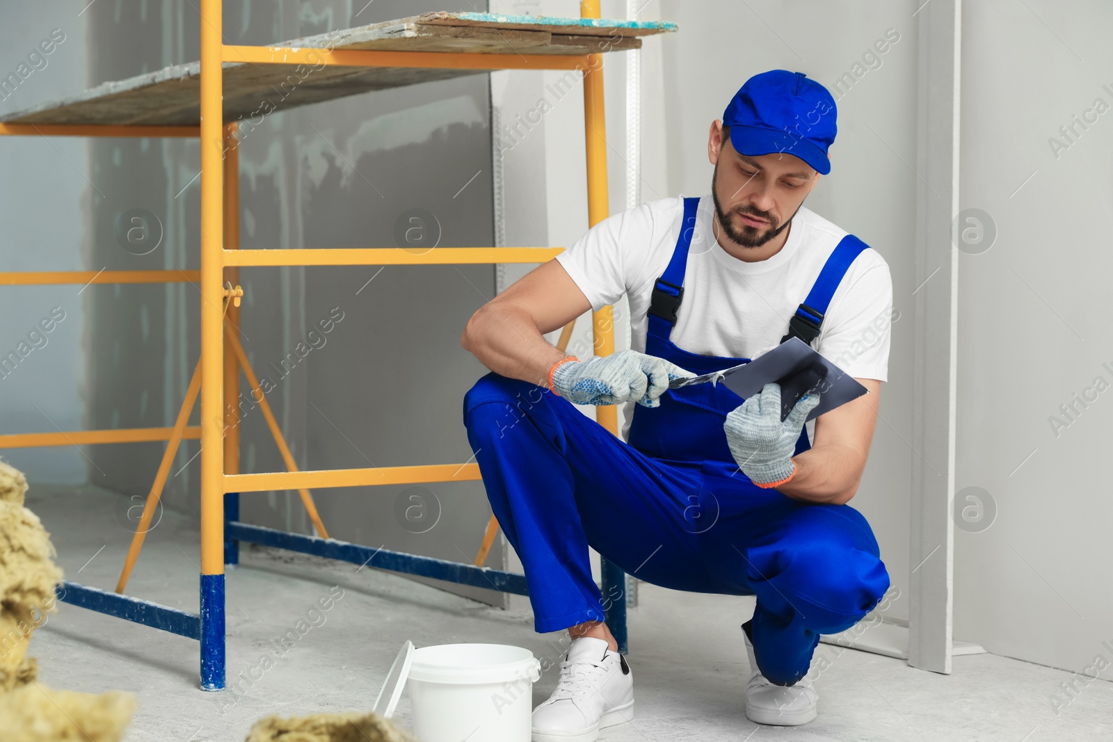 Photo of Professional worker putting plaster on putty knife indoors