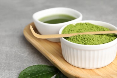 Green matcha powder, bamboo scoop and leaf on light grey table, closeup