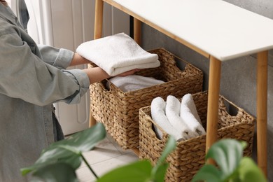 Woman putting towel into storage basket indoors, closeup