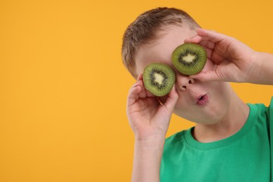 Photo of Emotional boy covering eyes with halves of fresh kiwi on orange background, space for text