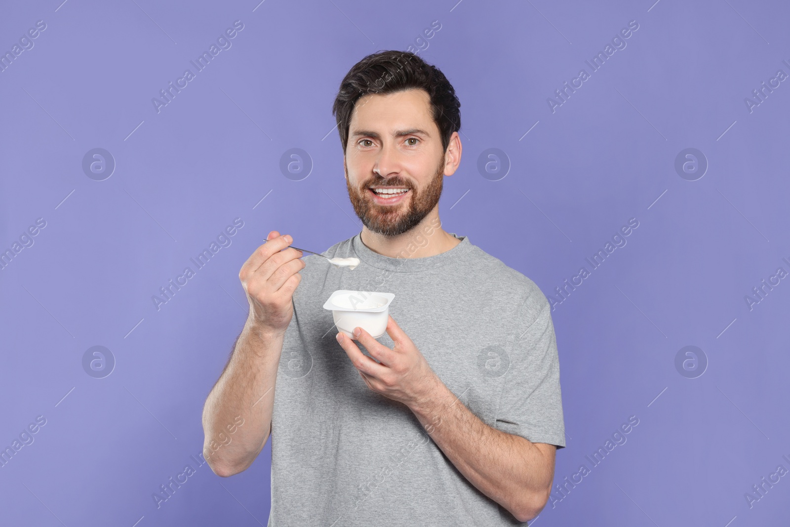 Photo of Handsome man with delicious yogurt and spoon on violet background