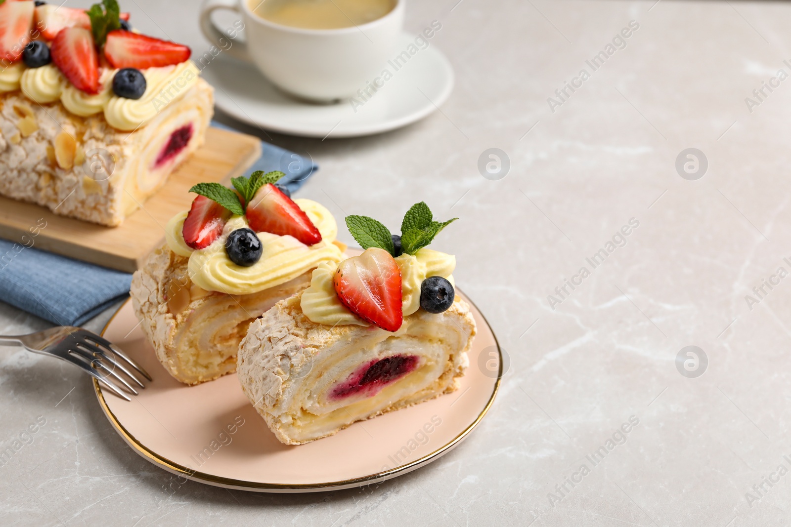 Photo of Tasty meringue roll with jam, cream, strawberry, blueberry and mint on light grey marble table, space for text