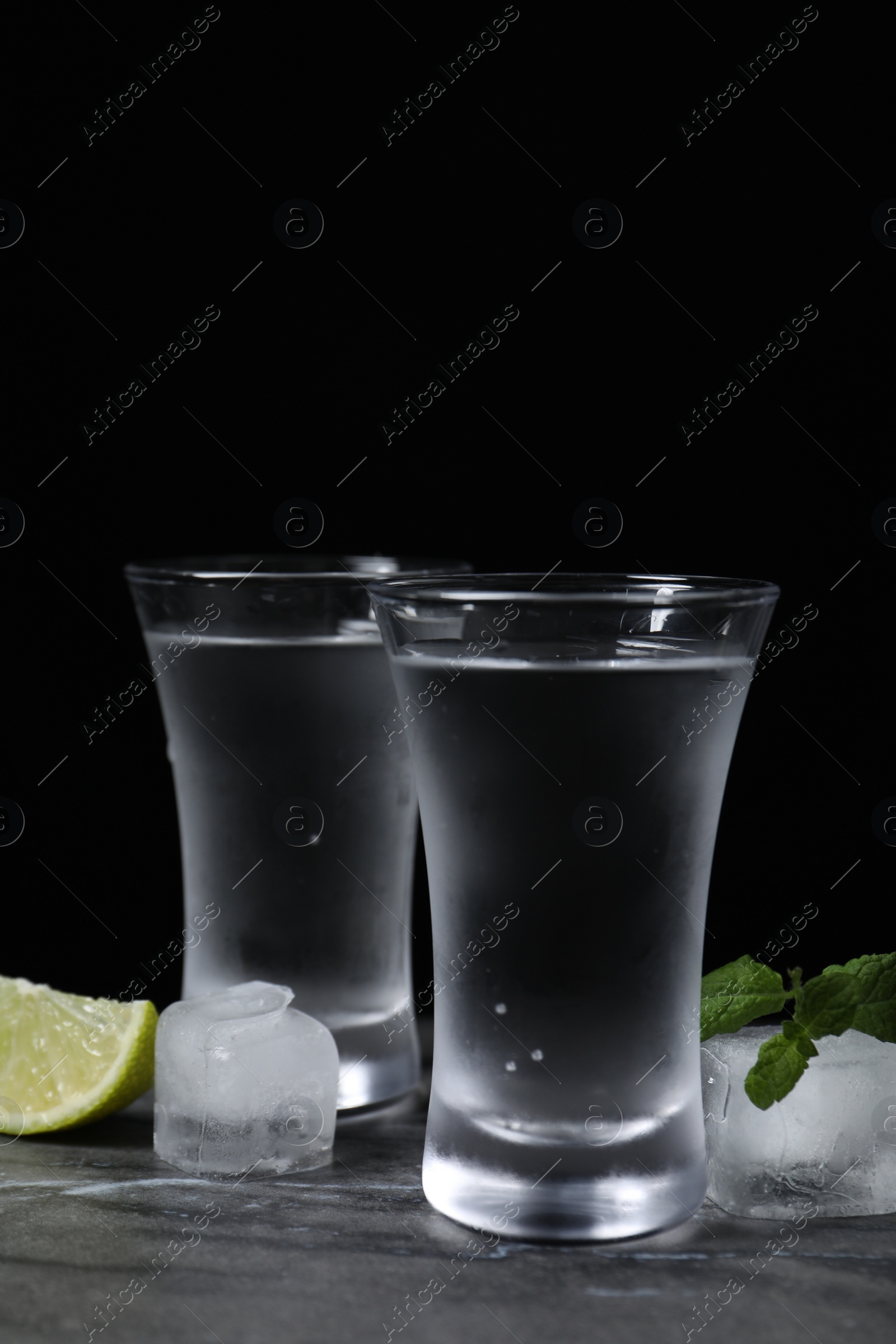 Photo of Shot glasses of vodka with lime slice, ice and mint on grey table