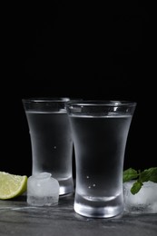 Photo of Shot glasses of vodka with lime slice, ice and mint on grey table
