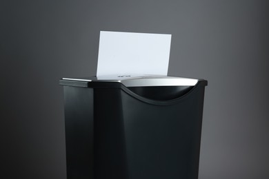 Shredder with sheet of paper on grey background